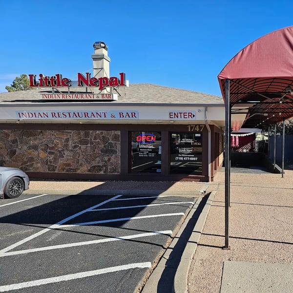 Exterior of Little Nepal Indian Restaurant & Bar with a stone facade and red awning.
