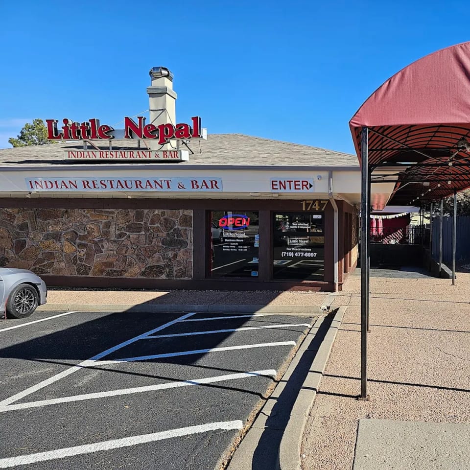 Exterior of Little Nepal Indian Restaurant & Bar with a stone facade and red awning.