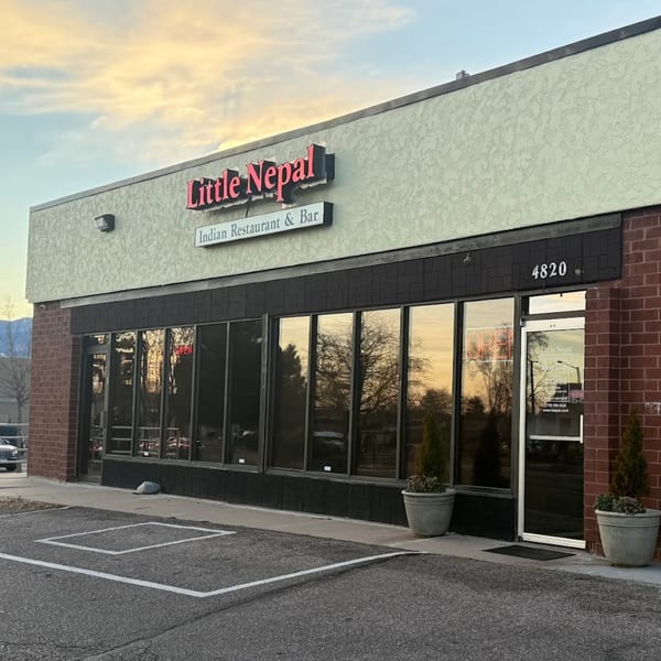 Exterior of Little Nepal Indian Restaurant & Bar with a red sign and large windows reflecting the sky.