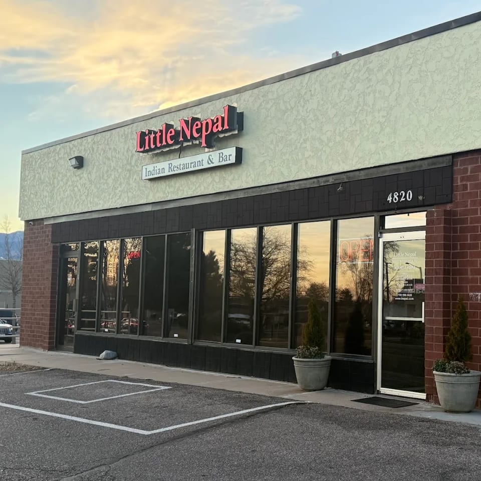 Exterior of Little Nepal Indian Restaurant & Bar with a red sign and large windows reflecting the sky.