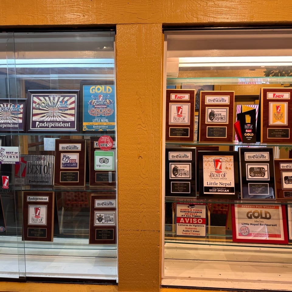 A display case filled with numerous awards and plaques for Little Nepal restaurant.