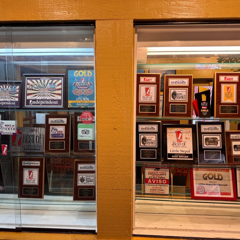 A display case filled with numerous awards and plaques for Little Nepal restaurant.