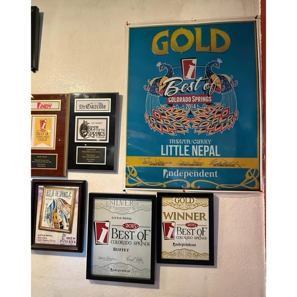 A wall displays multiple framed awards, including "Best of Colorado Springs" for Little Nepal restaurant.