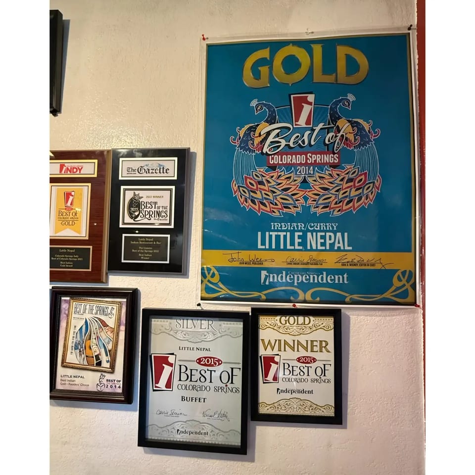 A wall displays multiple framed awards, including "Best of Colorado Springs" for Little Nepal restaurant.
