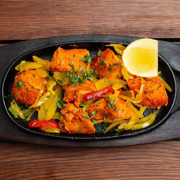 Indian chicken tikka with bell peppers, cilantro, and a lemon wedge on a sizzling platter.