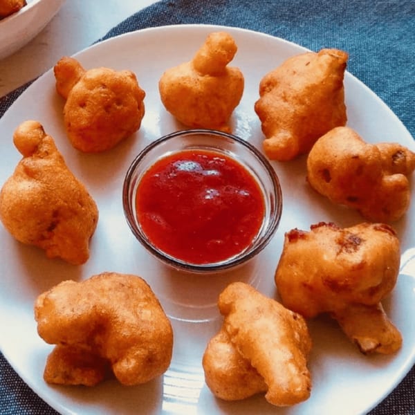 Golden-fried Indian pakoras, or vegetable fritters, arranged around a small bowl of red dipping sauce.